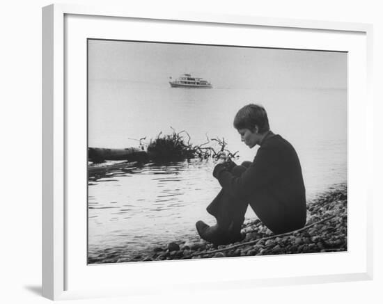 Actress Mia Farrow Pensively Sitting on Rocky Shore of Lake Geneva as Passenger Boat Passes By-Bill Eppridge-Framed Premium Photographic Print