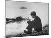 Actress Mia Farrow Pensively Sitting on Rocky Shore of Lake Geneva as Passenger Boat Passes By-Bill Eppridge-Mounted Premium Photographic Print