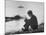 Actress Mia Farrow Pensively Sitting on Rocky Shore of Lake Geneva as Passenger Boat Passes By-Bill Eppridge-Mounted Premium Photographic Print