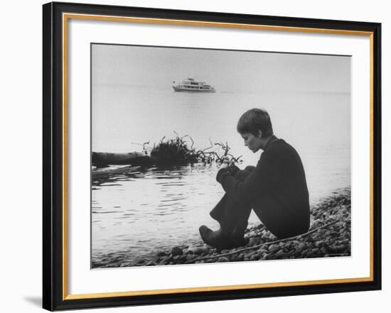 Actress Mia Farrow Pensively Sitting on Rocky Shore of Lake Geneva as Passenger Boat Passes By-Bill Eppridge-Framed Premium Photographic Print