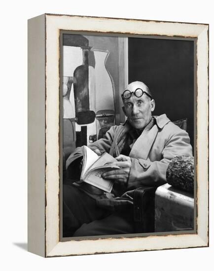 Architect Le Corbusier Sitting in Chair and Holding Book in Hands-Nina Leen-Framed Premier Image Canvas