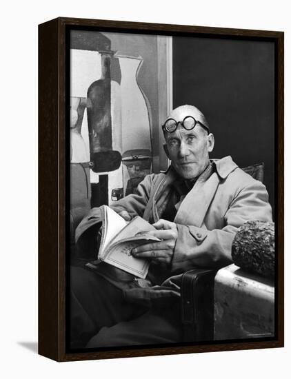 Architect Le Corbusier Sitting in Chair and Holding Book in Hands-Nina Leen-Framed Premier Image Canvas