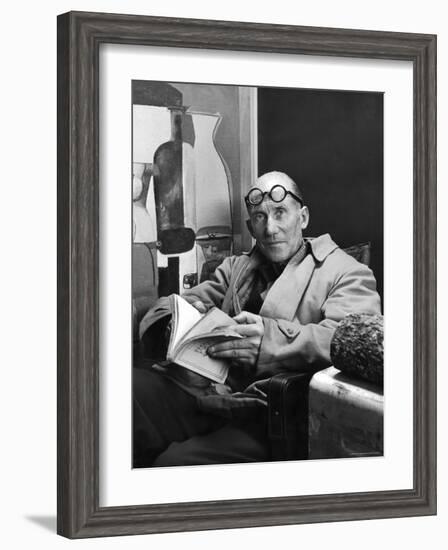 Architect Le Corbusier Sitting in Chair and Holding Book in Hands-Nina Leen-Framed Premium Photographic Print