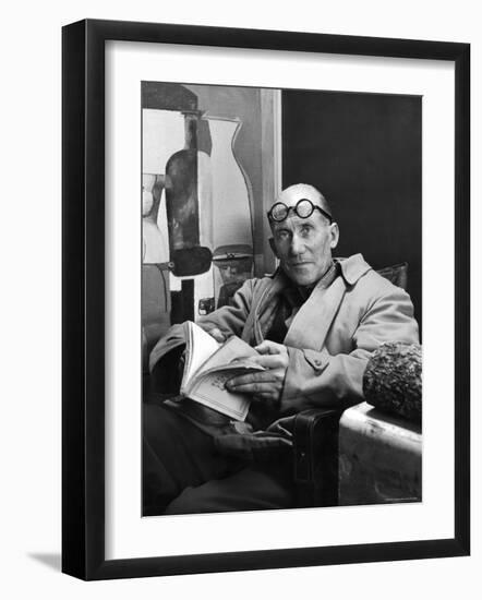 Architect Le Corbusier Sitting in Chair and Holding Book in Hands-Nina Leen-Framed Premium Photographic Print