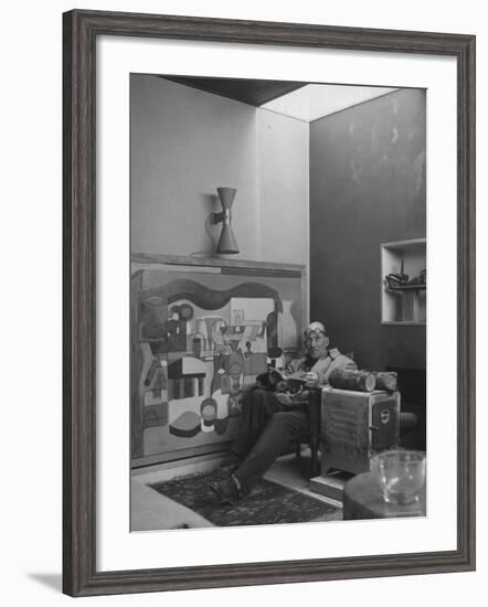 Architect Le Corbusier Sitting in Chair with Book in Hands, Glasses Perched on His Forehead-Nina Leen-Framed Premium Photographic Print