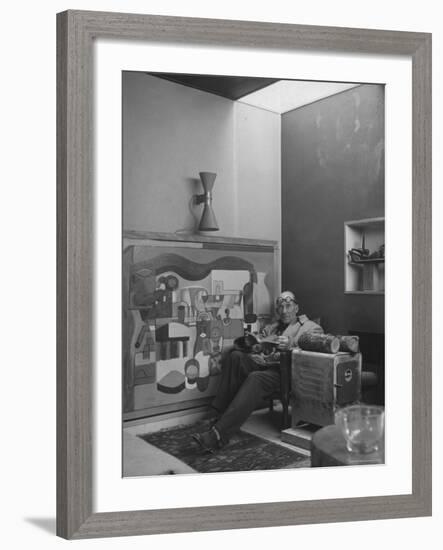 Architect Le Corbusier Sitting in Chair with Book in Hands, Glasses Perched on His Forehead-Nina Leen-Framed Premium Photographic Print