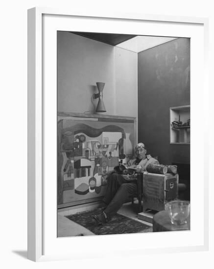 Architect Le Corbusier Sitting in Chair with Book in Hands, Glasses Perched on His Forehead-Nina Leen-Framed Premium Photographic Print