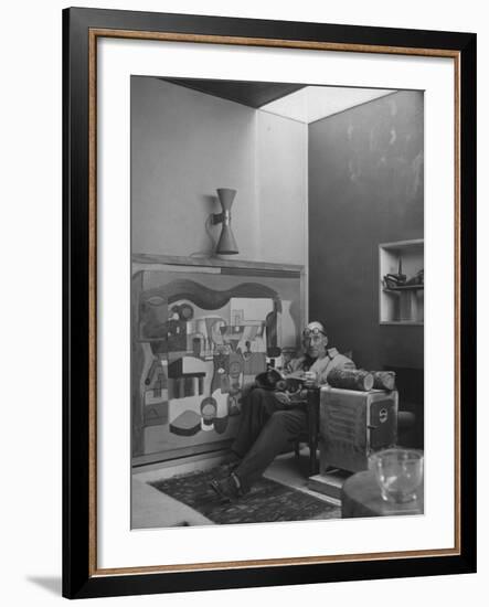 Architect Le Corbusier Sitting in Chair with Book in Hands, Glasses Perched on His Forehead-Nina Leen-Framed Premium Photographic Print