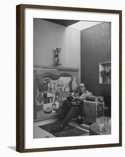 Architect Le Corbusier Sitting in Chair with Book in Hands, Glasses Perched on His Forehead-Nina Leen-Framed Premium Photographic Print