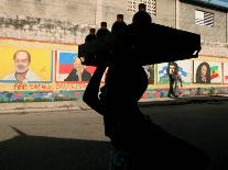 A Boy Carrying Bottles on His Head Passes by a Wall with Pictures of Haitian President Renel Preval-Ariana Cubillos-Premier Image Canvas