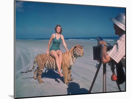 Bathing Beauty Sitting on Back of Large Tiger on Beach as Photographer Sets Up Camera-Eliot Elisofon-Mounted Photographic Print