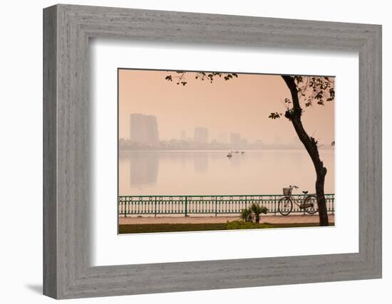 Bicycle parked at the lakeside with city skyline in the background, West Lake, Tay Ho, Hanoi, Vi...-null-Framed Photographic Print