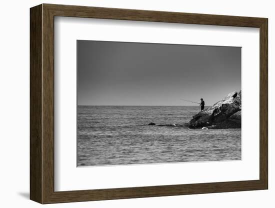 Black and White shot of a lone fisherman on rocks at the beach-null-Framed Photo