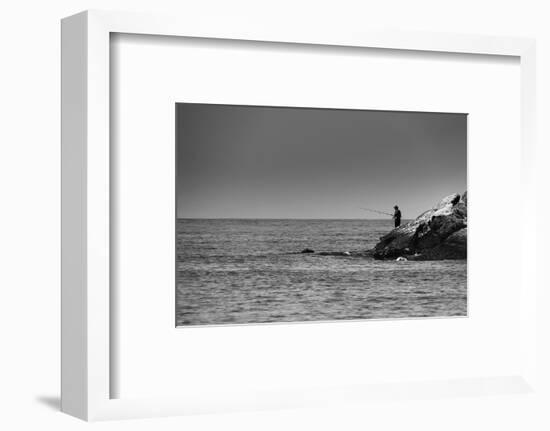 Black and White shot of a lone fisherman on rocks at the beach-null-Framed Photo