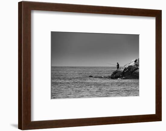 Black and White shot of a lone fisherman on rocks at the beach-null-Framed Photo