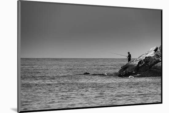 Black and White shot of a lone fisherman on rocks at the beach-null-Mounted Photo