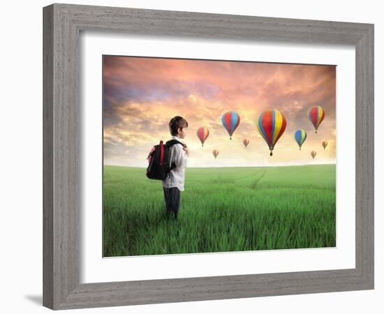 Child Carrying A Backpack Standing On A Green Meadow With Hot-Air Balloons In The Background-olly2-Framed Art Print