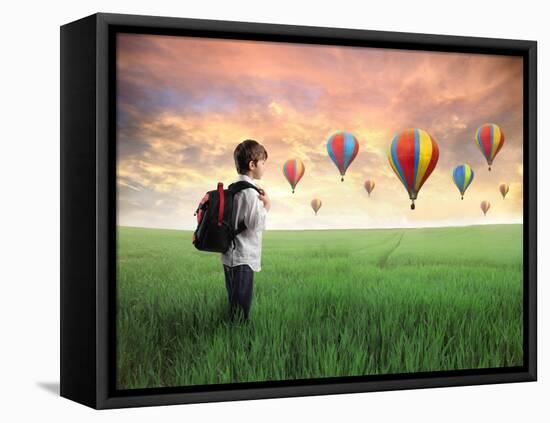 Child Carrying A Backpack Standing On A Green Meadow With Hot-Air Balloons In The Background-olly2-Framed Stretched Canvas