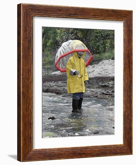 Child in Rain Gear with Umbrella Playing in Puddle.-Nora Hernandez-Framed Giclee Print