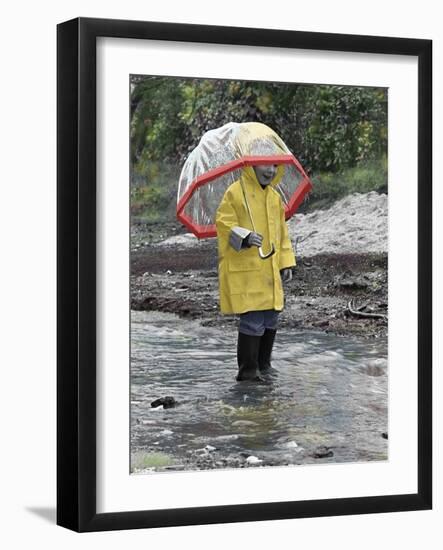 Child in Rain Gear with Umbrella Playing in Puddle.-Nora Hernandez-Framed Giclee Print