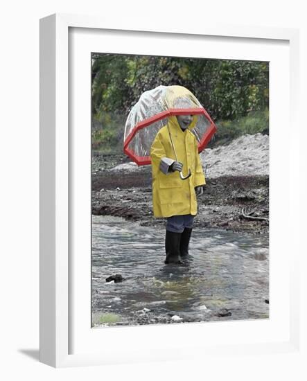 Child in Rain Gear with Umbrella Playing in Puddle.-Nora Hernandez-Framed Giclee Print