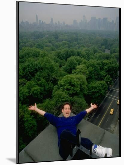 Comedian Jerry Seinfeld Perching Precariously on Roof Ledge Overlooking Central Park-Ted Thai-Mounted Premium Photographic Print