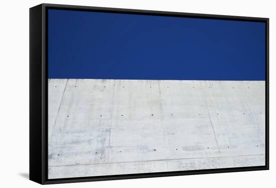 Concrete grey wall with structure and inclusions as a background in front of sky blue cloudless-Axel Killian-Framed Stretched Canvas