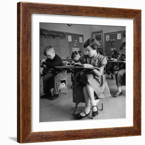 Cute Little Girl Busily at Work, Sitting in a Desk Chair in a Schoolroom, Other Pupils at Work Too-Gordon Parks-Framed Photographic Print