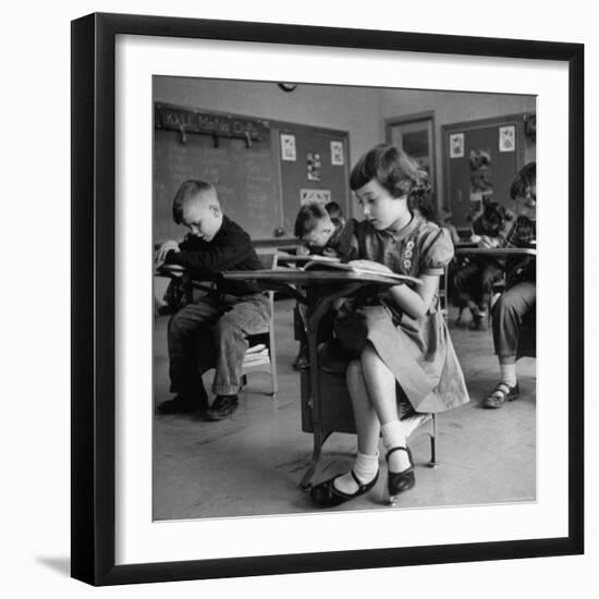 Cute Little Girl Busily at Work, Sitting in a Desk Chair in a Schoolroom, Other Pupils at Work Too-Gordon Parks-Framed Photographic Print