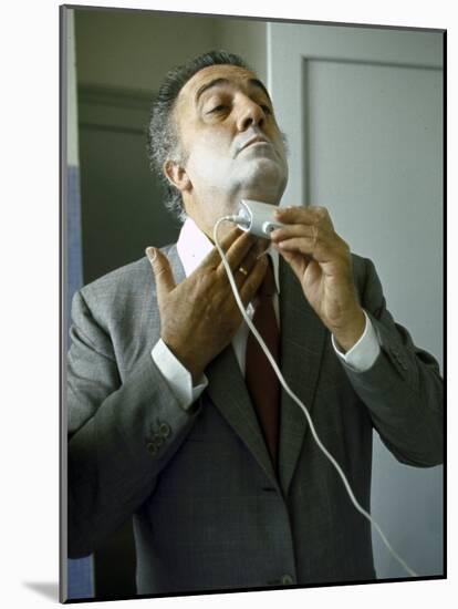 Director Federico Fellini with Powder on His Face as He Shaves with an Electric Shaver-Carlo Bavagnoli-Mounted Photographic Print