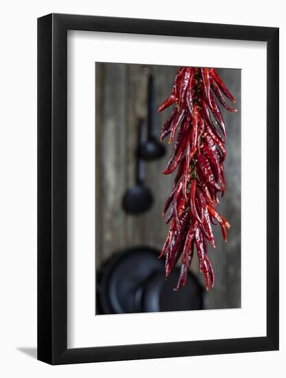 Dried Chillipods Hang Infront of Wooden Wall with Culinary Utensils-Jana Ihle-Framed Photographic Print