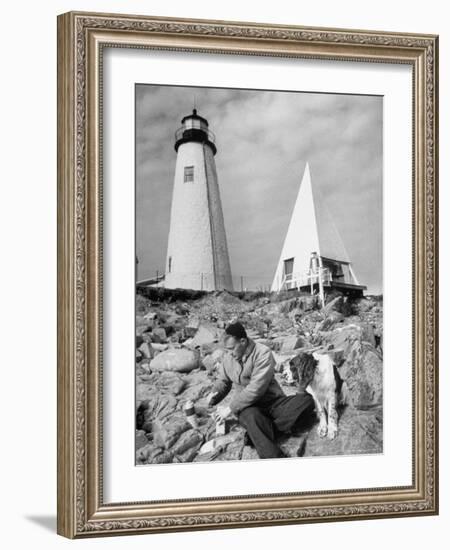 Eddie Frank Preparing to Eat Lunch on Rocks Next to His Dog in Front of Lighthouse-Alfred Eisenstaedt-Framed Photographic Print