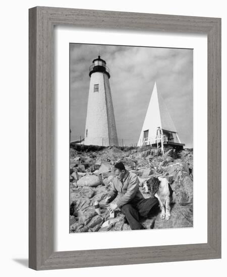 Eddie Frank Preparing to Eat Lunch on Rocks Next to His Dog in Front of Lighthouse-Alfred Eisenstaedt-Framed Photographic Print