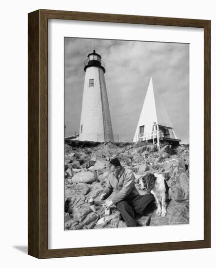 Eddie Frank Preparing to Eat Lunch on Rocks Next to His Dog in Front of Lighthouse-Alfred Eisenstaedt-Framed Photographic Print