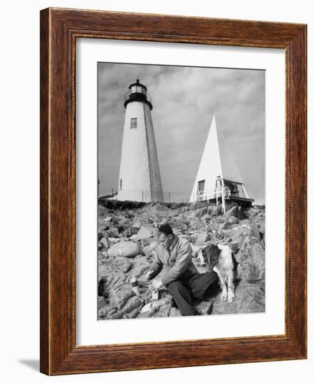 Eddie Frank Preparing to Eat Lunch on Rocks Next to His Dog in Front of Lighthouse-Alfred Eisenstaedt-Framed Photographic Print