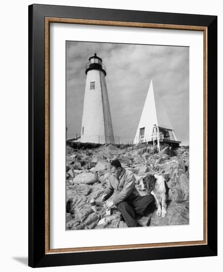 Eddie Frank Preparing to Eat Lunch on Rocks Next to His Dog in Front of Lighthouse-Alfred Eisenstaedt-Framed Photographic Print