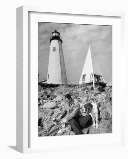 Eddie Frank Preparing to Eat Lunch on Rocks Next to His Dog in Front of Lighthouse-Alfred Eisenstaedt-Framed Photographic Print