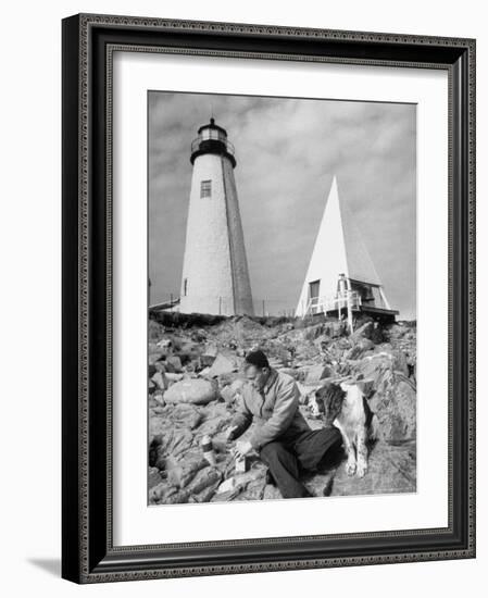 Eddie Frank Preparing to Eat Lunch on Rocks Next to His Dog in Front of Lighthouse-Alfred Eisenstaedt-Framed Photographic Print