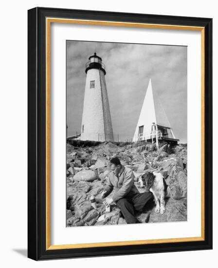 Eddie Frank Preparing to Eat Lunch on Rocks Next to His Dog in Front of Lighthouse-Alfred Eisenstaedt-Framed Photographic Print