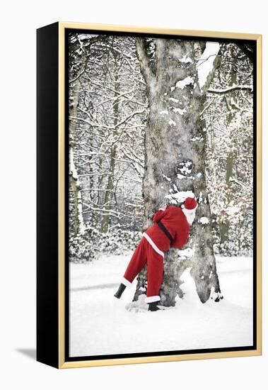 Father Christmas in Snow Behind Tree-null-Framed Premier Image Canvas