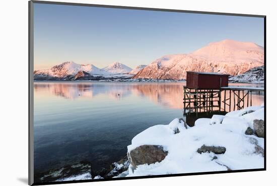 Fishing Hut on Stilts on a Pier, Winter Landscape in a Fjord in Front of Snowy Mountains-P. Kaczynski-Mounted Photographic Print