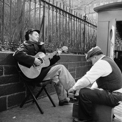 'Folk Singer Woody Guthrie Palying His Guitar While Getting a Shoeshine