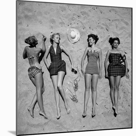 Four Models Showing Off the Latest Bathing Suit Fashions While Laying on a Sandy Florida Beach-Nina Leen-Mounted Photographic Print