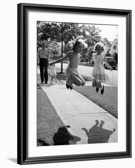 Girls on the street in neighborhood using rope to jump in tandem while man with toddler watches-Alfred Eisenstaedt-Framed Photographic Print