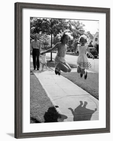 Girls on the street in neighborhood using rope to jump in tandem while man with toddler watches-Alfred Eisenstaedt-Framed Photographic Print