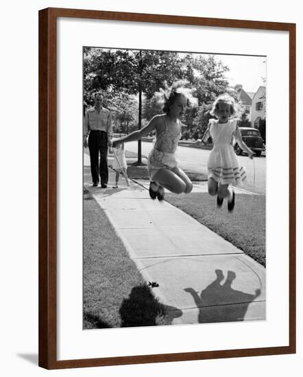 Girls on the street in neighborhood using rope to jump in tandem while man with toddler watches-Alfred Eisenstaedt-Framed Photographic Print