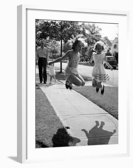 Girls on the street in neighborhood using rope to jump in tandem while man with toddler watches-Alfred Eisenstaedt-Framed Photographic Print