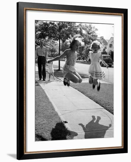 Girls on the street in neighborhood using rope to jump in tandem while man with toddler watches-Alfred Eisenstaedt-Framed Photographic Print