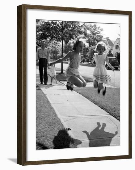 Girls on the street in neighborhood using rope to jump in tandem while man with toddler watches-Alfred Eisenstaedt-Framed Photographic Print