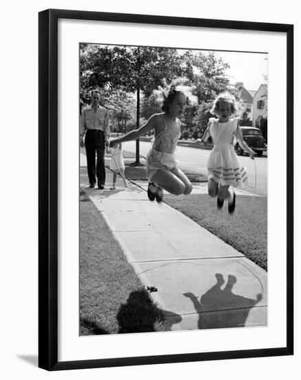 Girls on the street in neighborhood using rope to jump in tandem while man with toddler watches-Alfred Eisenstaedt-Framed Photographic Print